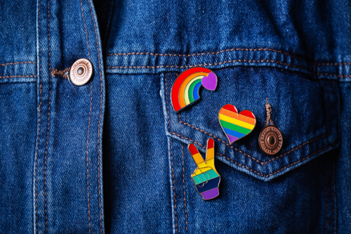 A close crop of a denim jacket with multiple LGBT flag and pride related pins